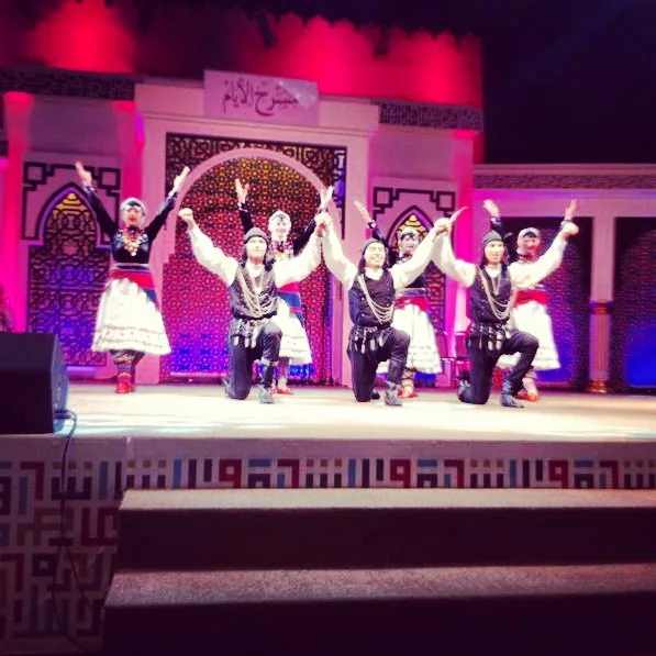 Salimcan performing in traditional costume on stage with a folk dance ensemble
